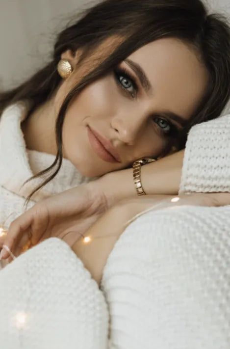 A model wearing 18k gold plated jewelry, including gold stud earrings and a gold bracelet