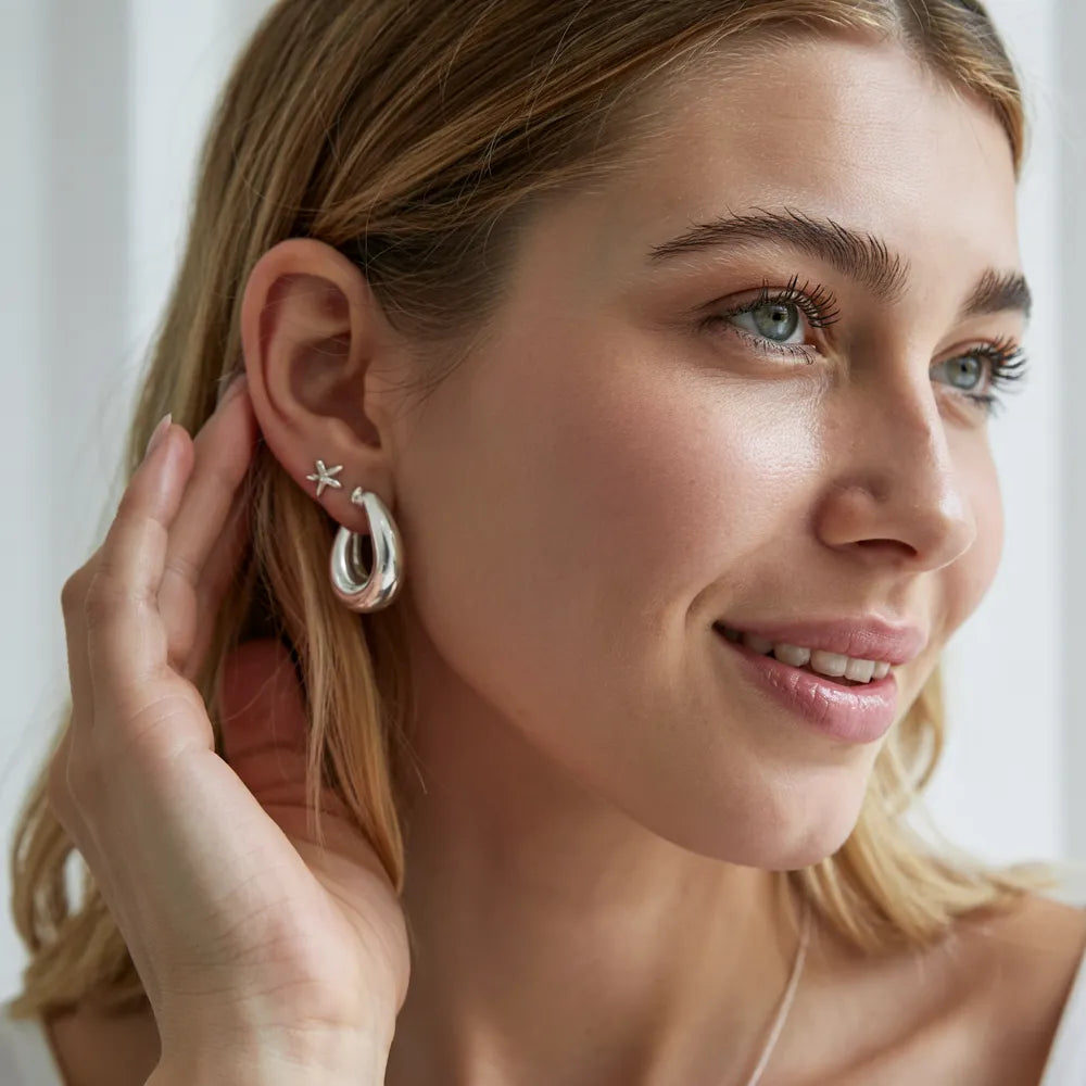 Image of a woman putting silver earrings in her ear