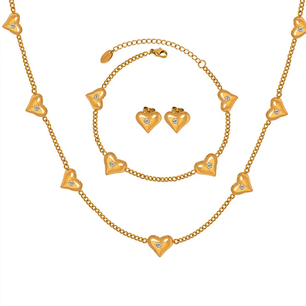 The complete Amara Solitaire Heart Jewelry Set in 18k gold, including the station necklace, bracelet, and stud earrings.