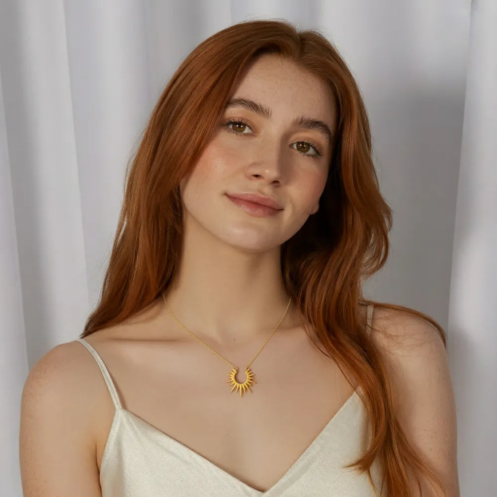 A model wearing the gold Helia sunburst pendant necklace with a white top, showcasing its style and length