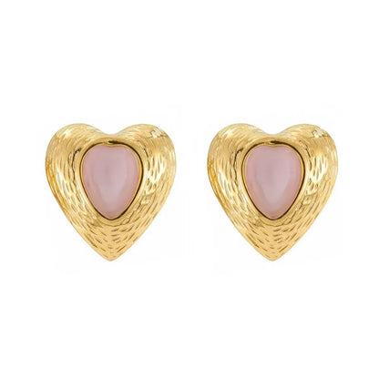 Pair of vintage-style 18K gold heart studs with a soft pink cat eye stone enclosed by a detailed gold border, against a white background.