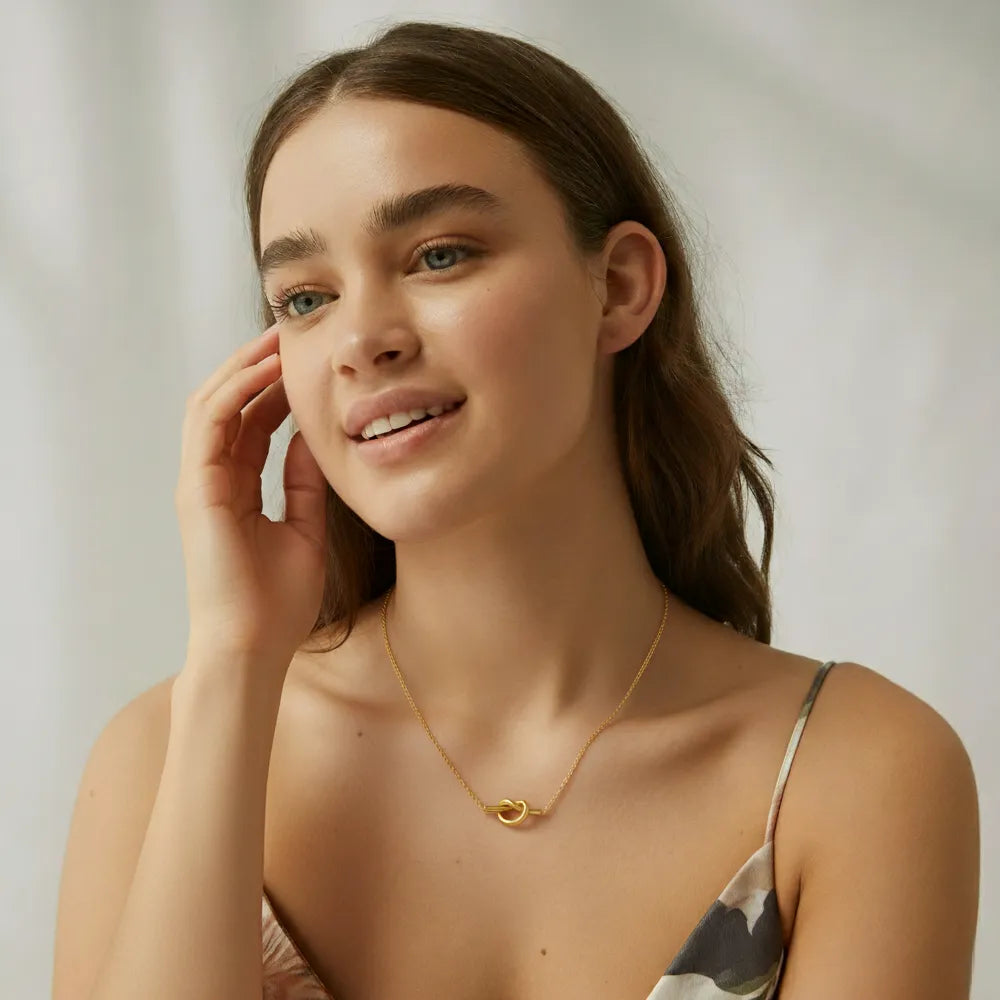 A model wearing the gold Elara Knot Heart Pendant necklace with a beige top to show its length and everyday style.