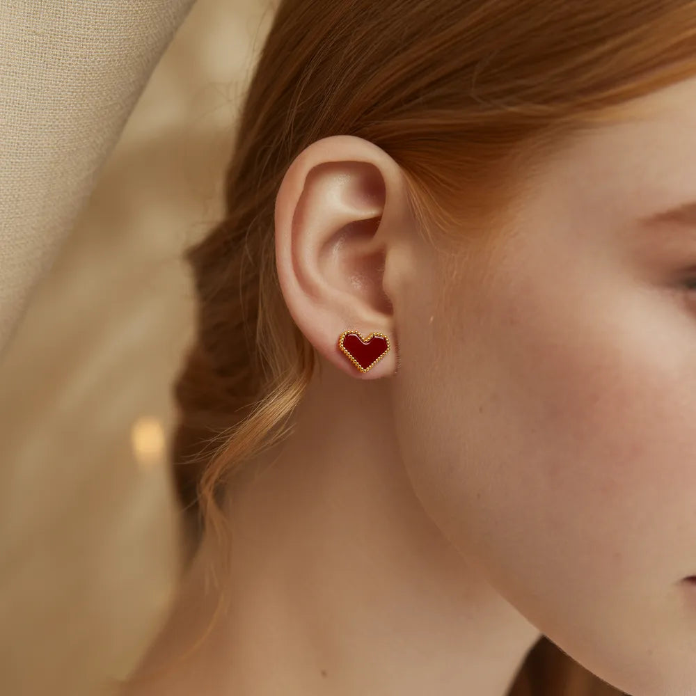Model wearing romantic red heart gold stud earrings featuring a beaded vintage edge.