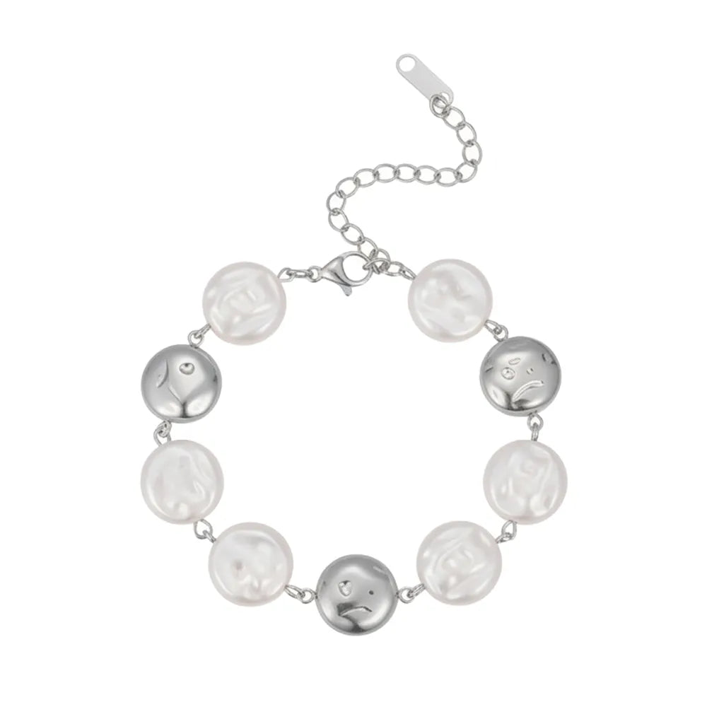 Silver stainless steel bracelet featuring irregular baroque pearls alternating with abstract sculpted face coins on a white background