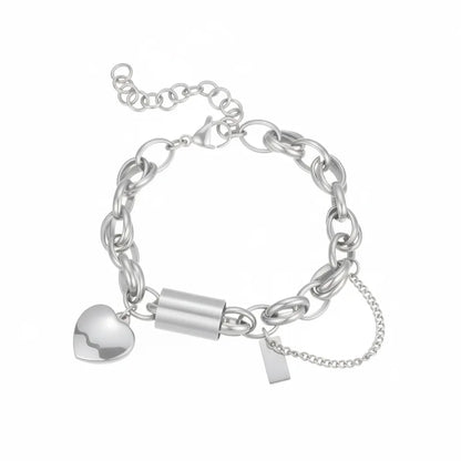 Silver stainless steel chain bracelet with a heart charm and rectangular tag detail, showing the lobster clasp and extender